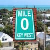 A view of key west homes, with a green sign in the middle that reads Mile 0, Key West.