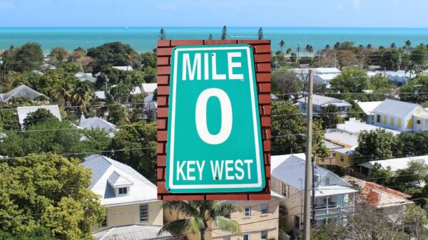 A view of key west homes, with a green sign in the middle that reads Mile 0, Key West.