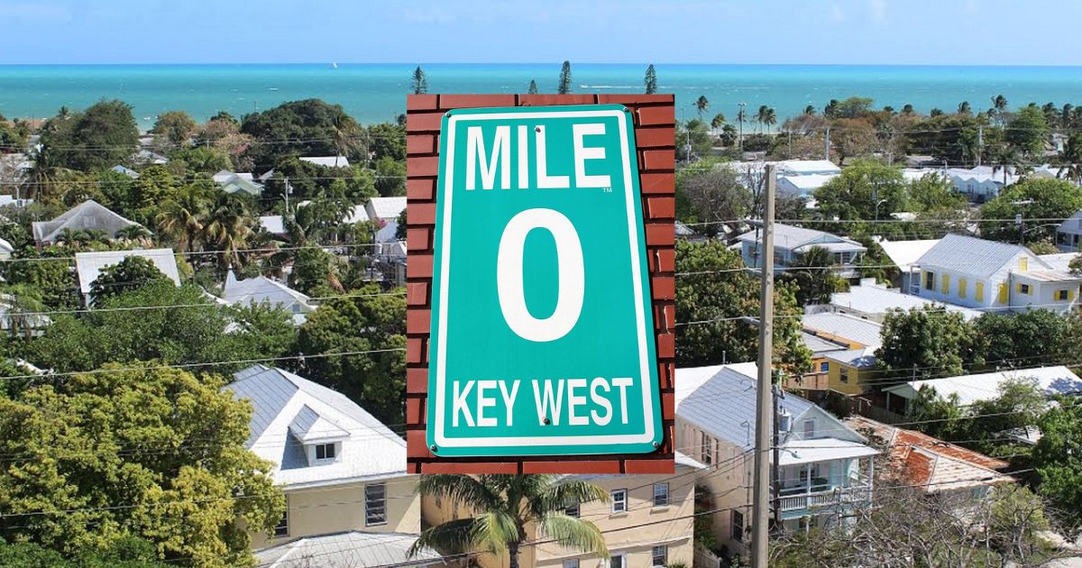 A view of key west homes, with a green sign in the middle that reads Mile 0, Key West.