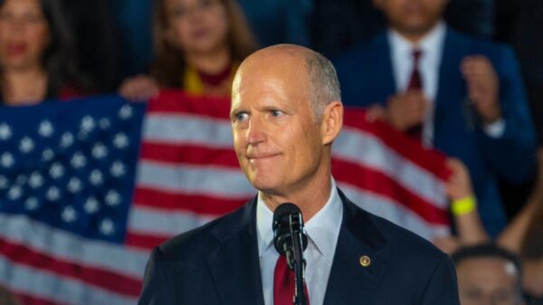 A picture of Florida Senator Rick Scott standing in front of a flag of the United States of America.