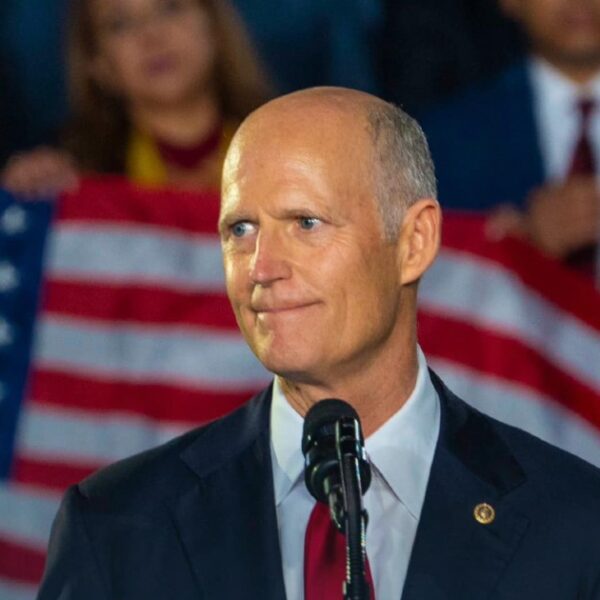 A picture of Florida Senator Rick Scott standing in front of a flag of the United States of America.