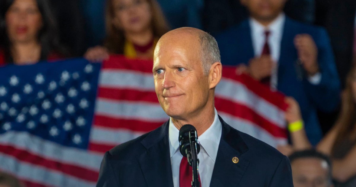 A picture of Florida Senator Rick Scott standing in front of a flag of the United States of America.